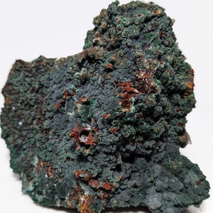 Puede incluir: Una roca rugosa de color verde y marrón con una superficie texturizada. La roca tiene una forma orgánica única y es un espécimen natural.