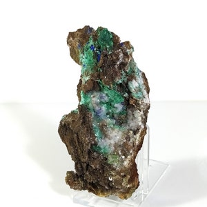 May include: A rough, brown rock with green and blue mineral deposits. The rock is on a clear acrylic stand.