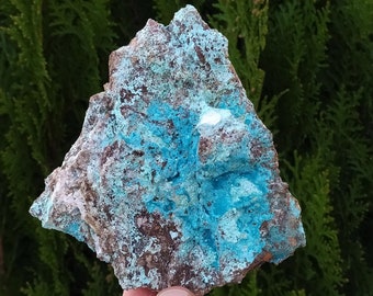 Puede incluir: Una roca rugosa de forma irregular con un revestimiento mineral azul verdoso. La roca se sostiene en una mano.