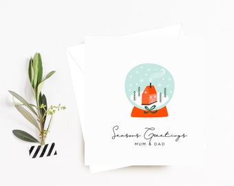 May include: A Christmas card featuring a snow globe illustration with a red house, chimney and smoke. The snow globe is on a red base with a green bow. The text "Seasons Greetings Mum & Dad" is printed below the snow globe.