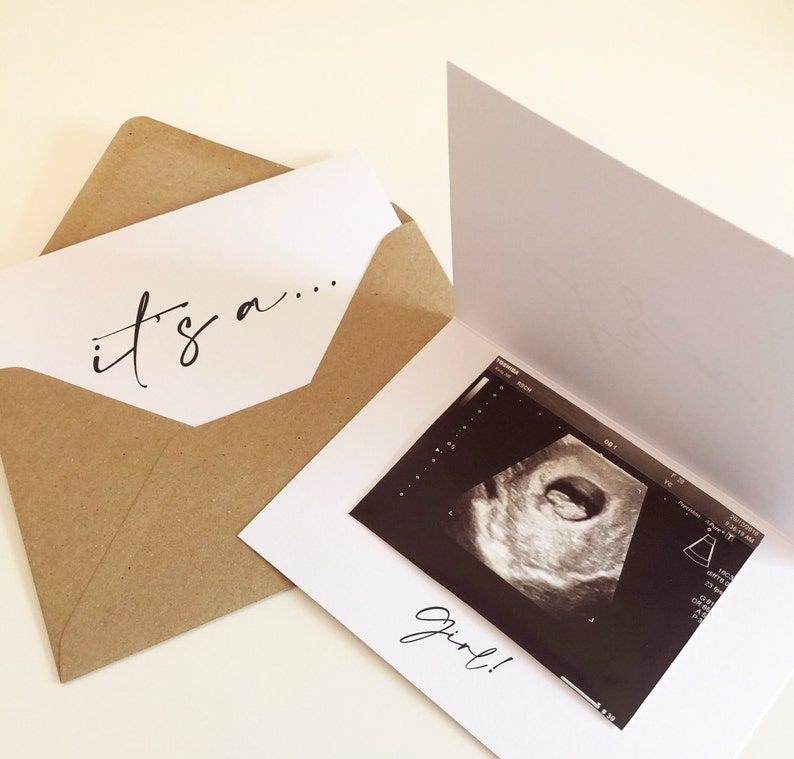 May include: A white card with the text "it's a..." on the front. The card is open to reveal a black and white ultrasound image with the text "girl!" below it.