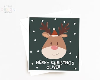 May include: A green Christmas card featuring a cartoon reindeer wearing a red Santa hat. The reindeer is surrounded by white dots against a dark green background. The text "Merry Christmas Oliver" is printed in white at the bottom of the card.