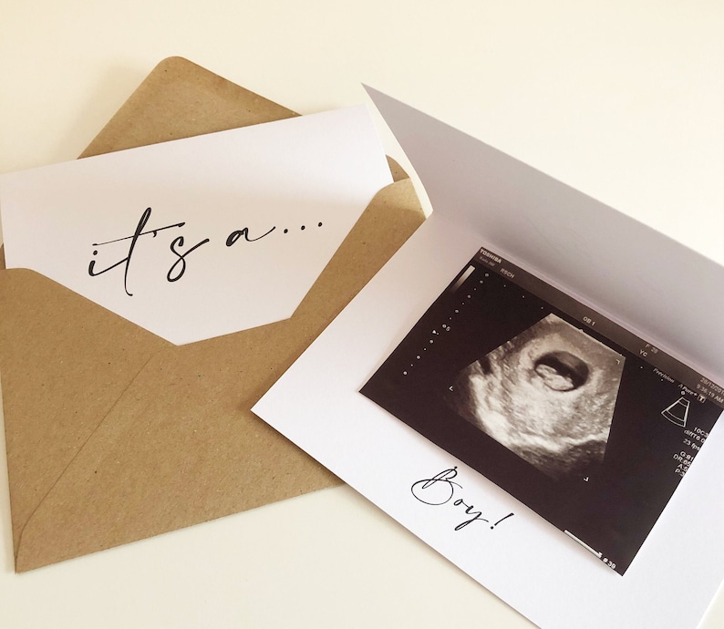 May include: A white card with the text "it's a..." on the front. The card is open to reveal a black and white ultrasound image with the text "Boy!" written below it.