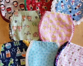 May include: A set of ten fabric baby bibs with crocheted trim. The bibs feature various patterns including penguins, reindeer, ducks, foxes, science, polka dots, and a grandma theme.