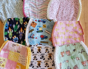 May include: Ten handmade baby bibs with different patterns and colors. The bibs are made of cotton fabric and have crocheted edges. The patterns include rockets, construction vehicles, animals, numbers, and polka dots.