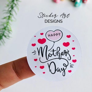 以下が含まれることがあります： ピンクのハートと黒い筆記体で「Happy Mother's Day」と書かれた白い丸いステッカー。ピンクの風船に「H.A.P.P.Y」と書かれており、テキストの上に浮かんでいます。
