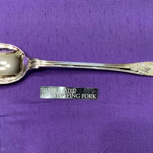 May include: Silver plated 13" stuffing fork with a decorative handle. The fork has three prongs and a spoon-like bowl.