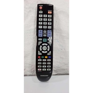 Op de afbeelding: Een zwarte Samsung tv-afstandsbediening met talrijke knoppen, waaronder aan/uit, kanaal, volume en menu. De afstandsbediening heeft een gebogen ontwerp en het Samsung-logo staat onderaan. De knoppen zijn wit.