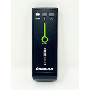 Puede incluir: Mando a distancia negro con detalles verdes. Cuenta con botones etiquetados como "POWER", "IR" e "INFO". Un gráfico verde indica "SOURCE". También se ve el texto "WIRELESS 3D-HD KIT" y el logotipo "IOGEAR".