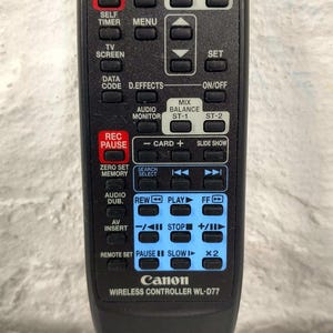 May include: Black Canon wireless controller WL-D77 with multiple buttons for various functions, including start/stop, zoom, menu, and audio controls. The remote has a rectangular shape and is designed for ease of use.