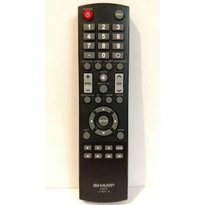 May include: A black Sharp TV remote control with numerous buttons. The remote features a red power button, number keys, volume and channel controls, and an enter button. The brand name "SHARP" is printed at the bottom.
