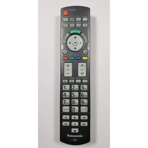 Op de afbeelding: Een donkergrijze Panasonic tv-afstandsbediening met een rode aan-uitknop, een centraal navigatiepaneel met een OK-knop, een groene VIERA CAST-knop, volume- en kanaalbediening, een numeriek toetsenblok en afspeelknoppen aan de onderzijde.
