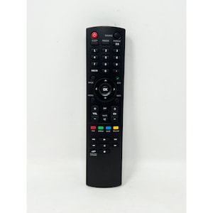 Op de afbeelding: Een zwarte tv-afstandsbediening met talrijke knoppen, waaronder aan/uit, kanaal, volume en cijfertoetsen. De afstandsbediening heeft een strak ontwerp met duidelijk gemarkeerde functies en gekleurde knoppen. Het woord "SOURCE" is bovenaan zichtbaar.