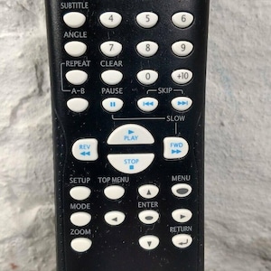 May include: Black DVD player remote control with white buttons and text. Features buttons for audio, subtitle, angle, repeat, pause, play, skip, and more. Includes the text "DVD VIDEO" and model number NB093.