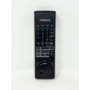 Puede incluir: Mando a distancia Hitachi negro con múltiples botones y un dial. El mando tiene botones para encendido, alarma, reposo, silencio, canal y volumen. La marca "HITACHI" está impresa en la parte superior.