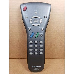 Puede incluir: Mando a distancia gris para televisor LCD Sharp con múltiples botones, incluyendo encendido, menú, volumen y control de canales. El mando tiene la marca "SHARP" y el número de modelo G1664CESB.
