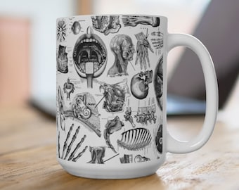 Könnte beinhalten: Weiße Keramiktasse mit einem Schwarzweiß-Druck einer anatomischen Illustration. Der Druck zeigt verschiedene Körperteile, darunter Ohr, Mund und Knochen.