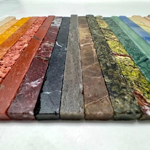 Könnte beinhalten: Eine Sammlung von 18 unterschiedlichfarbigen Marmorfliesenstreifen. Die Fliesen sind in einem Regenbogenmuster angeordnet, wobei die Farben von hellbeige bis dunkelgrün reichen.