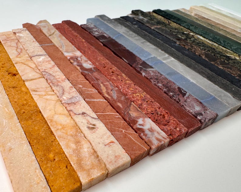 K&ouml;nnte beinhalten: Eine Sammlung rechteckiger Steinproben in verschiedenen Farben und Mustern. Die Proben umfassen Farbt&ouml;ne von Beige, Orange, Rot, Braun, Grau und Gr&uuml;n. Die Texturen variieren von glatt bis leicht rau und zeigen die nat&uuml;rlichen Variationen im Stein.