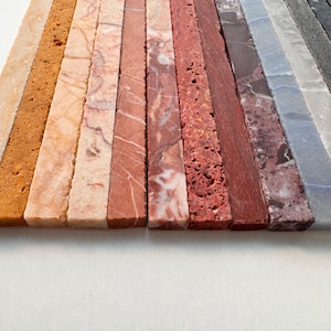 K&ouml;nnte beinhalten: Eine Ansammlung rechteckiger Steinfliesen in verschiedenen Farben und Texturen. Die Fliesen reichen von hellem Beige und Tan bis hin zu Orange-, Rot-, Grau- und Schwarzt&ouml;nen. Die Oberfl&auml;chen weisen nat&uuml;rliche Muster und Variationen auf.