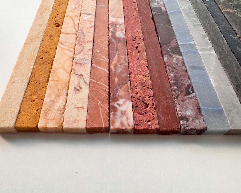 K&ouml;nnte beinhalten: Eine Ansammlung rechteckiger Steinfliesen in verschiedenen Farben und Texturen. Die Fliesen reichen von hellem Beige und Tan bis hin zu Orange-, Rot-, Grau- und Schwarzt&ouml;nen. Die Oberfl&auml;chen weisen nat&uuml;rliche Muster und Variationen auf.