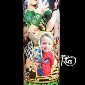 May include: A cylindrical tumbler featuring a collage of professional wrestlers, including John Cena in a green cap and wristbands, alongside a child holding a championship belt. The base displays the text MONEY IN THE BANK and TARA'S CREATIVE Flow.