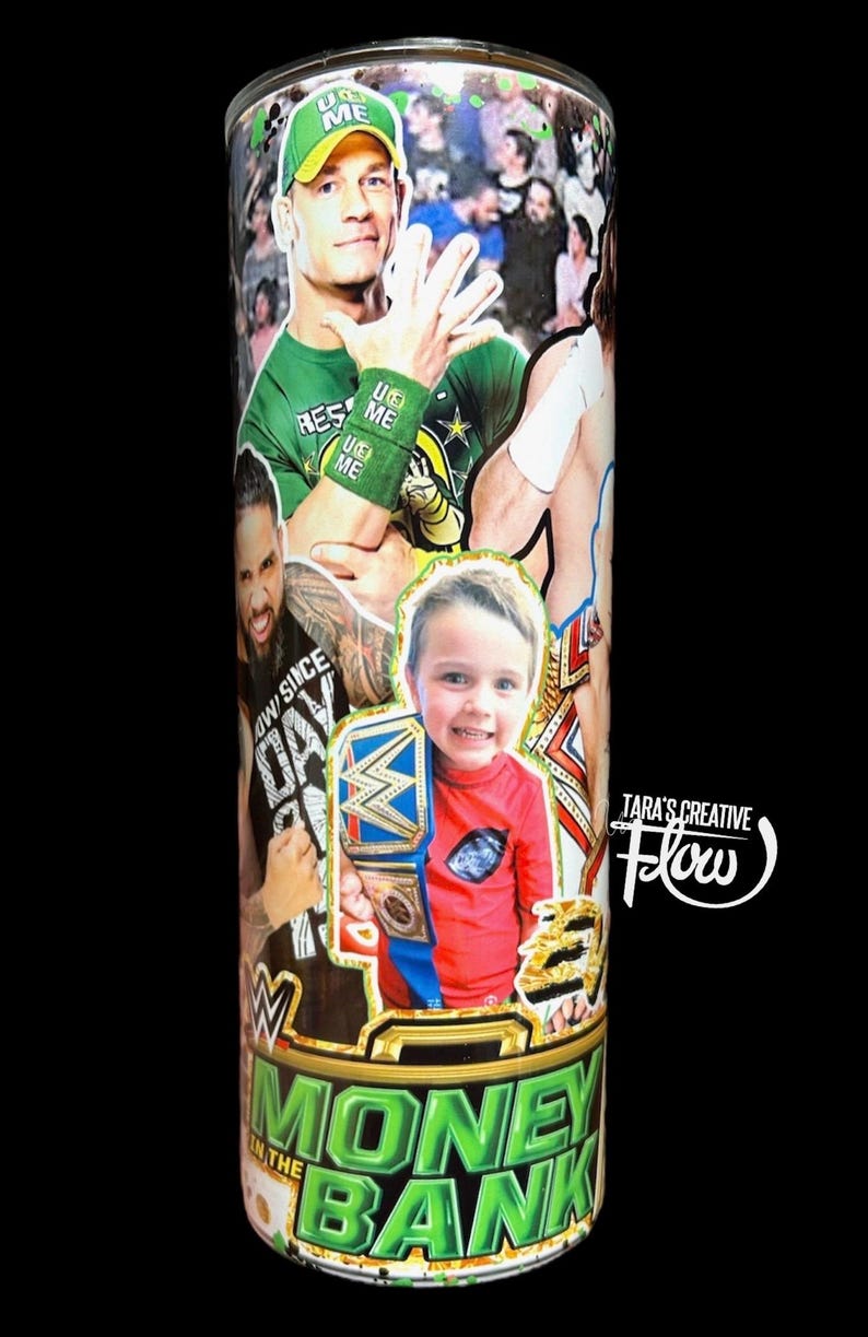 May include: A cylindrical tumbler featuring a collage of professional wrestlers, including John Cena in a green cap and wristbands, alongside a child holding a championship belt. The base displays the text MONEY IN THE BANK and TARA'S CREATIVE Flow.