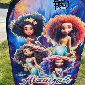 May include: A backpack featuring a vibrant underwater scene with four animated mermaid characters with curly hair. The design includes the text "Tara's Creative Flow" at the top and the name "Aizayah" in stylized blue and gold lettering at the bottom.