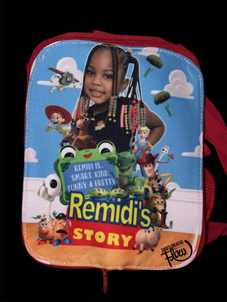 May include: A rectangular red lunch bag featuring a custom graphic print of a child surrounded by animated toy characters. The text reads: REMIDI IS... SMART, KIND, FUNNY & PRETTY, REMIDI'S STORY, and TARA'S CREATIVE FLOW. The background is blue.
