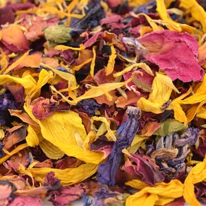 May include: A close-up of a mixture of dried flower petals in shades of yellow, pink, purple, and blue. The petals are arranged in a random pattern, creating a colorful and textured background.