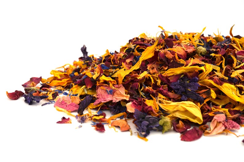May include: A pile of dried flower petals in shades of yellow, orange, red, pink, and blue. The petals are scattered on a white background.