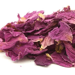 May include: A pile of dried rose petals in shades of pink and purple against a white background. The petals vary in size and texture, with some showing hints of yellow and brown.