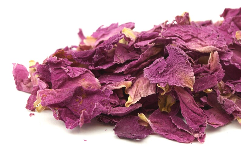 May include: A pile of dried rose petals in shades of pink and purple against a white background. The petals vary in size and texture, with some showing hints of yellow and brown.