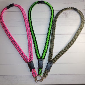May include: Three paracord lanyards featuring a braided design with black plastic side-release buckles and metal swivel clips. The lanyards are colored in neon pink with purple accents, neon green with black, and a solid olive green camouflage pattern.