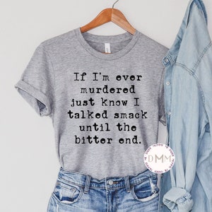 K&ouml;nnte beinhalten: Ein graues T-Shirt mit dem Text "If I'm ever murdered just know I talked smack until the bitter end." Das Shirt wird mit Jeansshorts und einem hellblauen Jeanshemd kombiniert. Das T-Shirt h&auml;ngt an einem Holzb&uuml;gel.