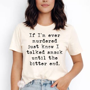 K&ouml;nnte beinhalten: Cremefarbenes T-Shirt mit schwarzem Text: "If I'm ever murdered just know I talked smack until the bitter end." Das kurz&auml;rmelige Shirt wird mit einer blauen Jeans getragen.