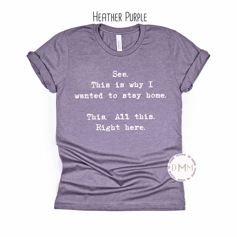 May include: Heather purple t-shirt with the text "See. This is why I wanted to stay home. This. All this. Right here." The shirt has rolled-up sleeves and a crew neck.