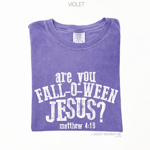 Puede incluir: Una camiseta violeta de manga corta con un estampado gr&aacute;fico blanco desgastado que dice "are you FALL-O-WEEN JESUS?" seguido de "matthew 4:19". La prenda cuenta con un cuello redondo y una etiqueta de la marca Comfort Colors en el interior.