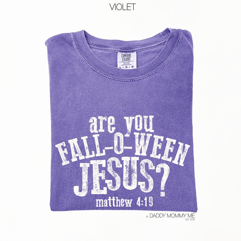 Puede incluir: Una camiseta violeta de manga corta con un estampado gr&aacute;fico blanco desgastado que dice "are you FALL-O-WEEN JESUS?" seguido de "matthew 4:19". La prenda cuenta con un cuello redondo y una etiqueta de la marca Comfort Colors en el interior.