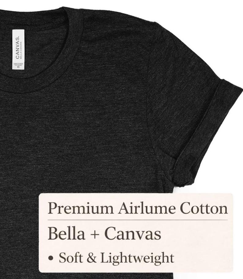 K&ouml;nnte beinhalten: Dunkelgraues T-Shirt mit hochgekrempelten &Auml;rmeln. Das Shirt hat einen Rundhalsausschnitt und ist aus einem weichen, leichten Material gefertigt. Das Etikett lautet "Premium Airlume Cotton", "Bella + Canvas" und "Soft & Lightweight".