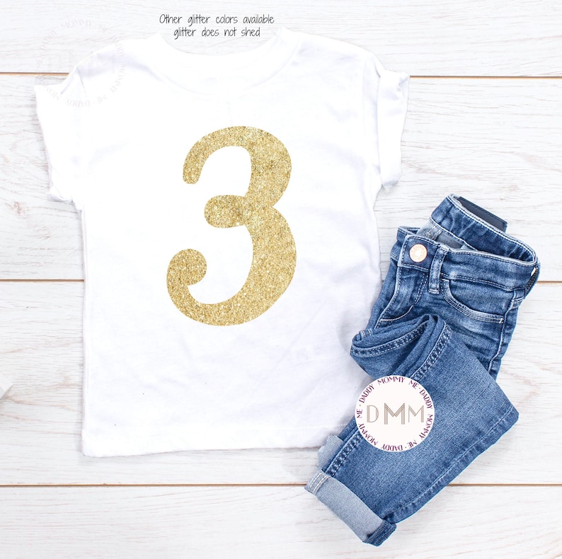 May include: White t-shirt with a large gold glitter number 3. The shirt is paired with folded blue denim jeans. Text at the top reads "Other glitter colors available glitter does not shed."
