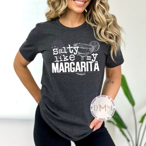 May include: A dark gray t-shirt with the text "Salty like my Margarita" in white. The text is accompanied by a drawing of a margarita glass with a lime wedge.