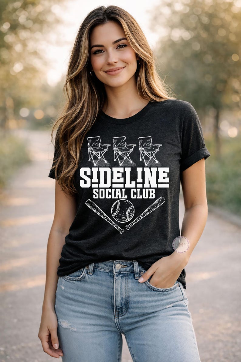 Op de afbeelding: Donkergrijs t-shirt met de witte tekst "SIDELINE SOCIAL CLUB", vergezeld van illustraties van klapstoelen, een honkbal en knuppels. De persoon draagt een blauwe spijkerbroek.
