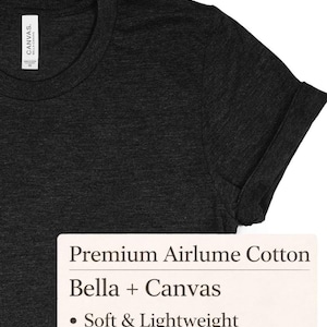 May include: Dark gray t-shirt with a rolled-up sleeve. The shirt has a crew neck and a tag on the inside collar. The text on the tag reads "Canvas" and "Bella + Canvas". The shirt is made of premium Airlume cotton and is soft and lightweight.