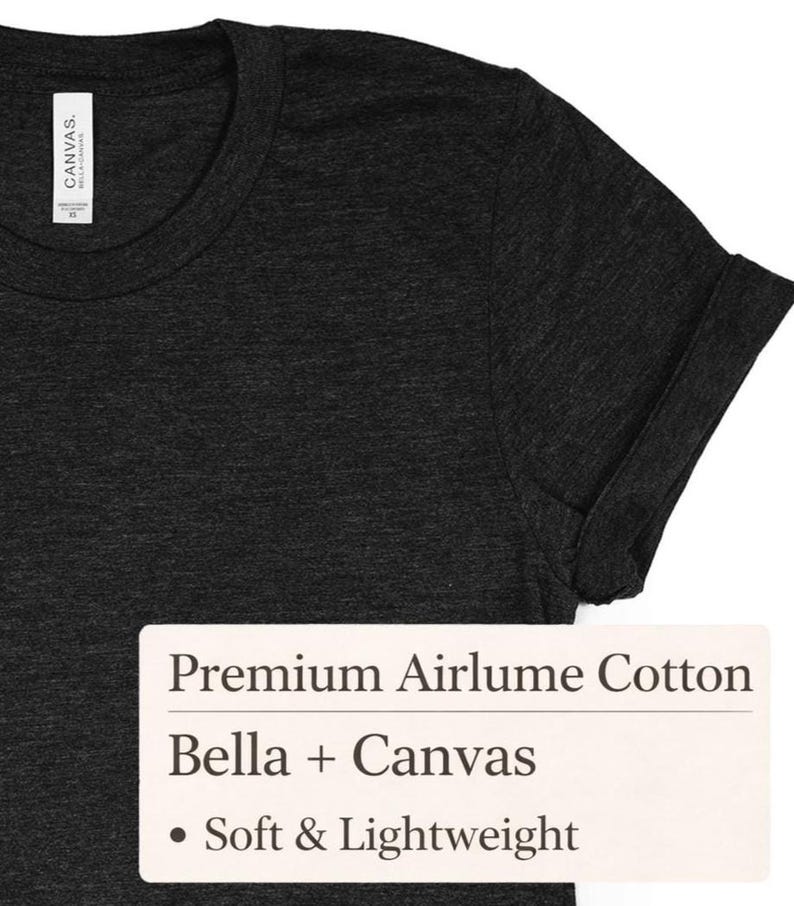 May include: Dark gray t-shirt with a rolled-up sleeve. The shirt has a crew neck and a tag on the inside collar. The text on the tag reads "Canvas" and "Bella + Canvas". The shirt is made of premium Airlume cotton and is soft and lightweight.