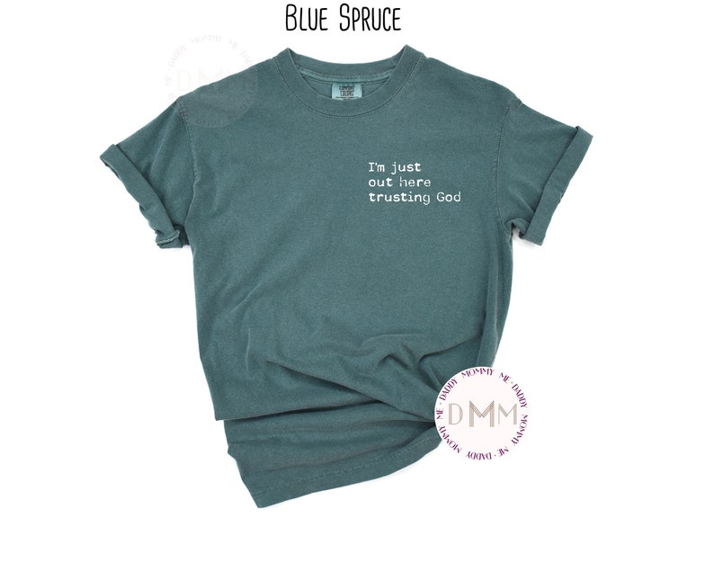 K&ouml;nnte beinhalten: Ein kurz&auml;rmeliges T-Shirt in der Farbe Blau-Fichte mit Rundhalsausschnitt. Auf der Vorderseite befindet sich auf der linken Brust ein wei&szlig;er Aufdruck mit dem Text, I'm just out here trusting God. Der Stoff wirkt leicht verwaschen und hat umgekrempelte &Auml;rmel.