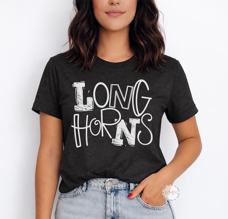 May include: Dark grey t-shirt featuring the white text "LONG HORNS" in a bold, outlined font. The short-sleeved shirt is made of a soft material. The shirt is worn by a person.
