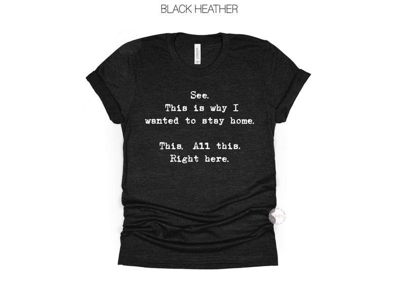 May include: Black heather t-shirt with the text "See. This is why I wanted to stay home. This. All this. Right here." The shirt has a V-neck and short sleeves. The text is in a simple, sans-serif font.