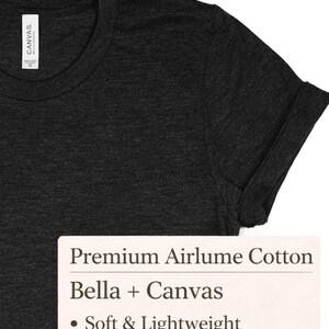 Op de afbeelding: Donkergrijs t-shirt met opgerolde mouwen. Het shirt heeft een ronde hals en een label met de tekst "Canvas". Een rechthoekig label toont de tekst "Premium Airlume Cotton", "Bella + Canvas" en "Soft & Lightweight".