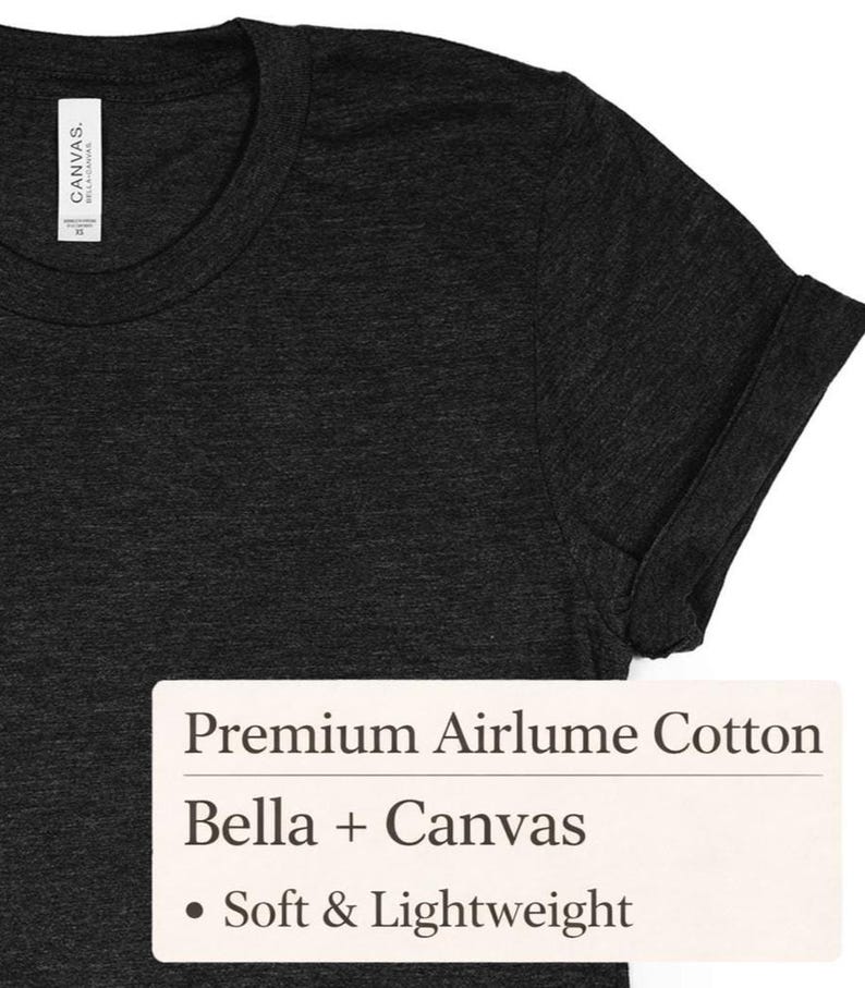 Op de afbeelding: Donkergrijs t-shirt met opgerolde mouwen. Het shirt heeft een ronde hals en een label met de tekst "Canvas". Een rechthoekig label toont de tekst "Premium Airlume Cotton", "Bella + Canvas" en "Soft & Lightweight".